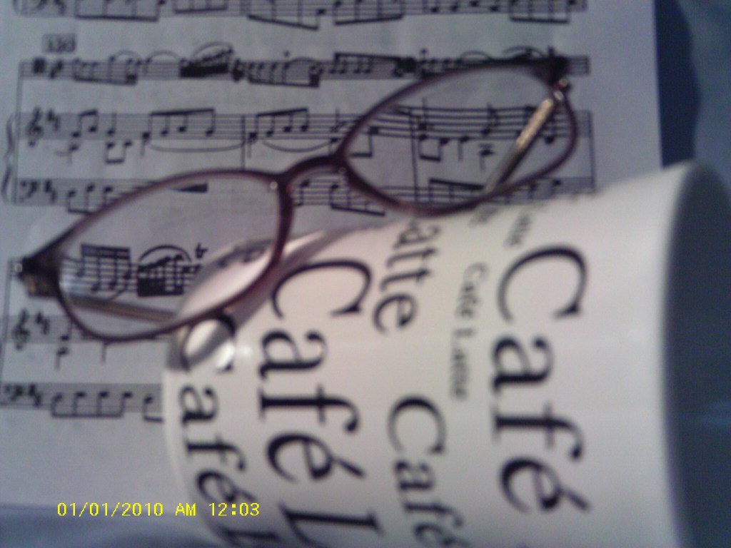 Music score with eyeglasses on top of cup on its side with Café Latte written on it.