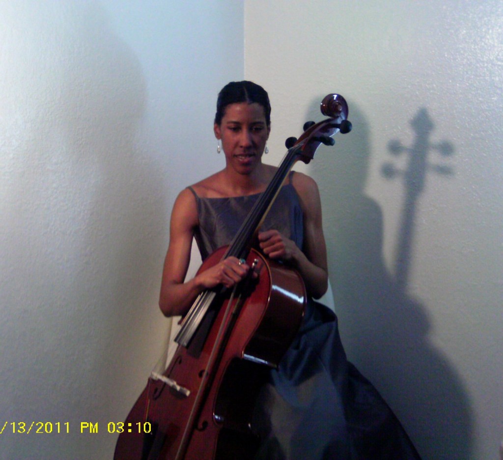 Margôt R. Hamilton Violoncelliste & Conceptual Designer seated with several shadow reflections in background from light